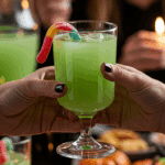 A hand holding an elegant glass of a homemade, green, and spooky "Ghostly" Punch at a fun and festive Halloween party.