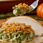 A beautiful plate of a homemade, elegant, and crispy-topped Green Bean Casserole, being served with a thick slice of a roasted turkey at a Thanksgiving dinner.
