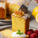 An elegant slice of homemade, moist, and glazed Lemon Pound Cake being served on a dessert plate with fresh raspberries.