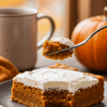A beautiful slice of homemade, moist, and frosted Pumpkin Bar being enjoyed with a fork and a cup of coffee on a cozy fall morning.