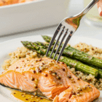 A healthy dinner plate with a serving of homemade, glazed Honey Mustard Baked Salmon, served with roasted asparagus and quinoa.