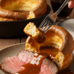 A beautiful plate of a homemade, puffy Yorkshire Pudding served with thick slices of a medium-rare roast beef and a rich, dark gravy at a family dinner.