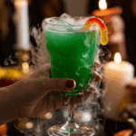 A hand holding an elegant glass of a homemade, green, and spooky "Witch's Brew" Punch at a fun and festive Halloween party.